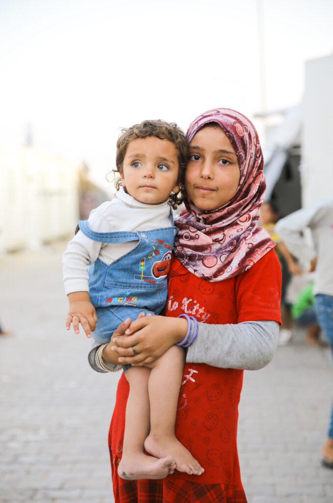 Muslimisches Kind mit Hijab hält ihre kleine Schwester auf dem Arm.