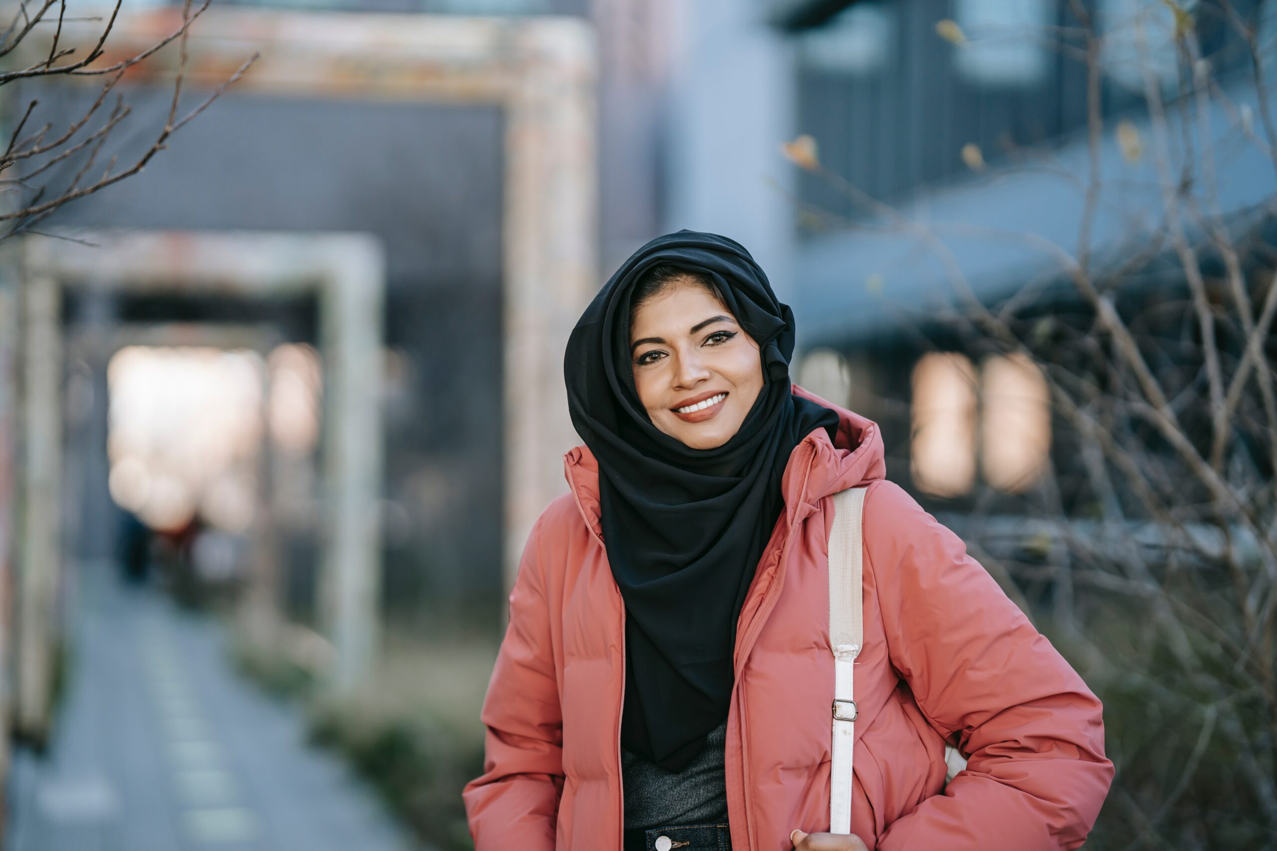 Eine junge muslimische Frau trägt einen Hijab und eine rosane Jacke.