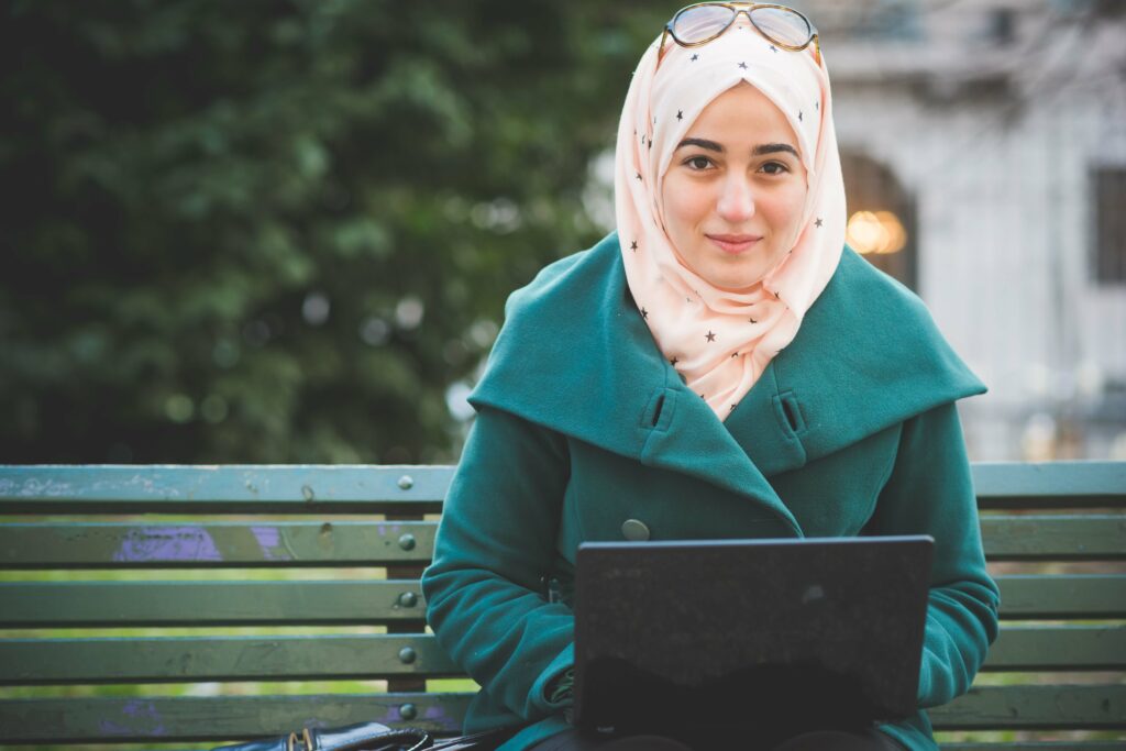 Junge muslimische Frau am Laptop schaut lächelnd in die Kamera.