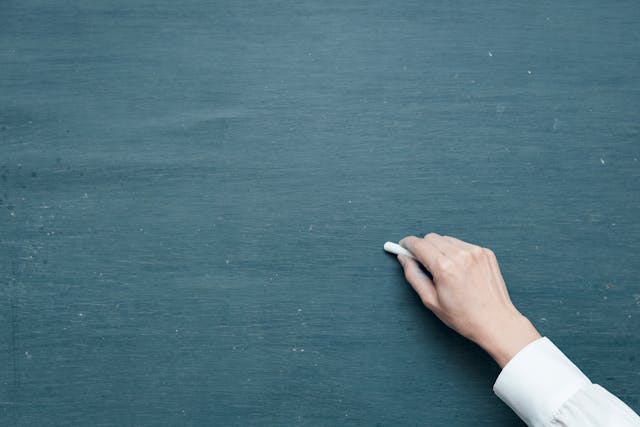 Eine Tafel, wie Sprachlehrer sie verwenden, und eine Hand, die ein weißes Stück Kreide hält.