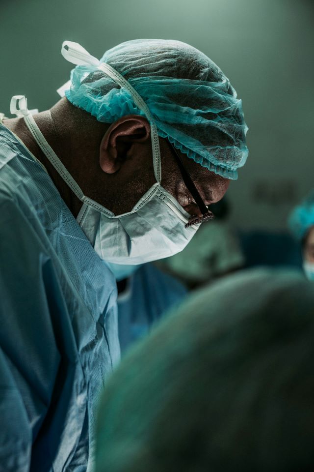Ein Chirurg oder eine andere medizinische Fachkraft in Schutzkleidung schaut konzentriert nach unten.